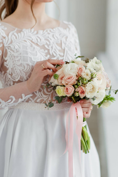 The wedding bouquet in the hands of the bride. The bride holds the bouquet. The wedding bouquet with ribbons.  - Foto, imagen