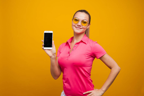 Bright and positive young woman with smartphone on yellow background. The girl uses a smartphone - Фото, изображение