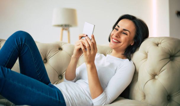 Lazy Sunday mood. Close-up photo of a happy girl in casual clothes who is smiling happily while texting with her significant other. - Zdjęcie, obraz