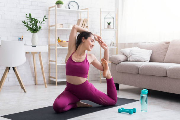 Quédate en casa, mantente en forma. Chica joven flexible haciendo yoga o ejercicios de estiramiento en la sala de luz
 - Foto, imagen