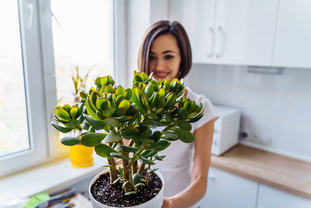 Horizontal photo, half-length plan. An attractive girl planted her big green flower into a new pot, holding it in her hands and admiring. Pleased with her work. Lifestyle concept of handmade work - Photo, image