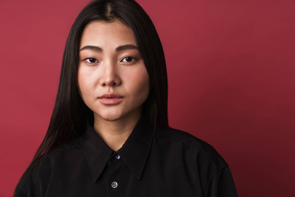 Close up of a pretty confident young asian woman wearing casual clothes standing isolated over red background, looking at camera - Fotoğraf, Görsel
