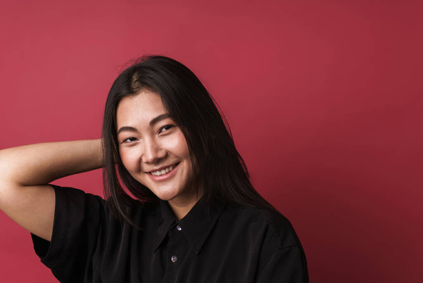 Close up of a pretty smiling young asian woman wearing casual clothes standing isolated over red background, looking at camera - 写真・画像