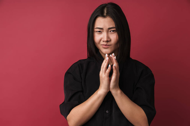 Close up of a pretty upset young asian woman wearing casual clothes standing isolated over red background - Foto, Imagen