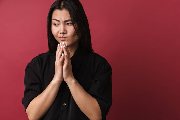 Close up of a pretty upset young asian woman wearing casual clothes standing isolated over red background - Zdjęcie, obraz