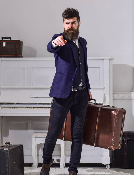 Man, traveller with beard and mustache with luggage, luxury white interior background. Baggage delivery concept. Macho elegant on strict face stands, holds suitcase, pointing forward. - Photo, Image