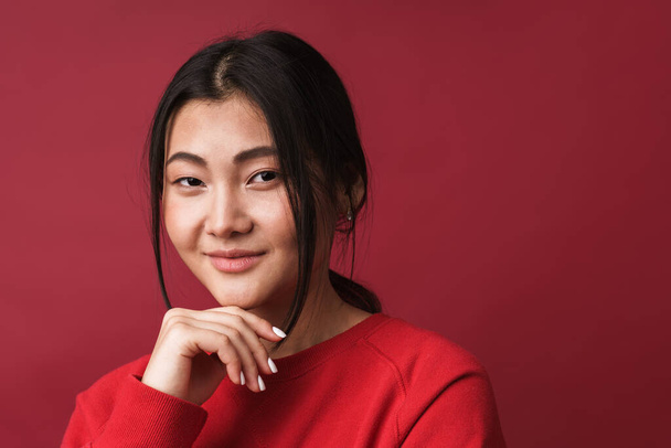 Close up of a pretty smiling young asian woman wearing casual clothes standing isolated over red background, looking at camera - Foto, immagini