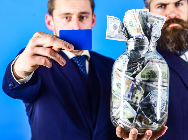 Banker, finance manager recommends to his client put money on bank account. Finance consultant concept. Businessmen with jar full of cash and credit card, blue background, close up, copy space. - Photo, image