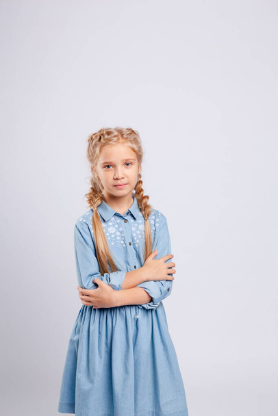 langhaarige Mädchen steht auf einem hellgrauen Hintergrund in einem blauen Kleid. - Foto, Bild
