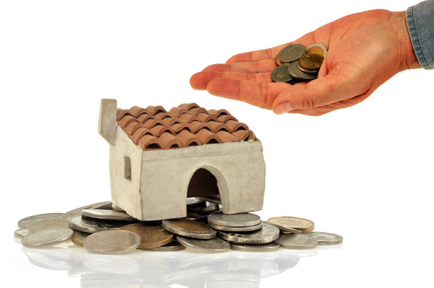 Έννοια χρηματοδοτικής συνεισφοράς με ένα σπίτι και ένα χέρι γεμάτο κέρματα από κοντά σε λευκό φόντο - Φωτογραφία, εικόνα