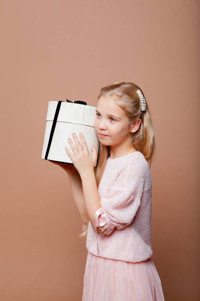 blondynka dziewczyna w różowy elegancki strój posiada pudełko ozdobione łukiem - Zdjęcie, obraz