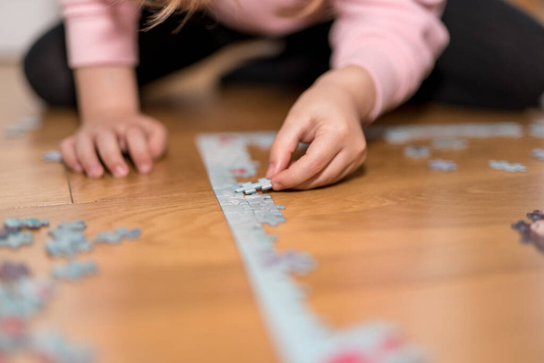 Blond girl in a pink sweater playing with a jigsaw on the floor by the confinement of coronavirus covid-19 - Fotografie, Obrázek