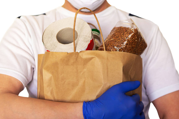 食品の顔マスクと手袋のハンドリングバッグを身に着けている男を提供。covid19中の郵便配達とエクスプレス食料品配達サービス. - 写真・画像