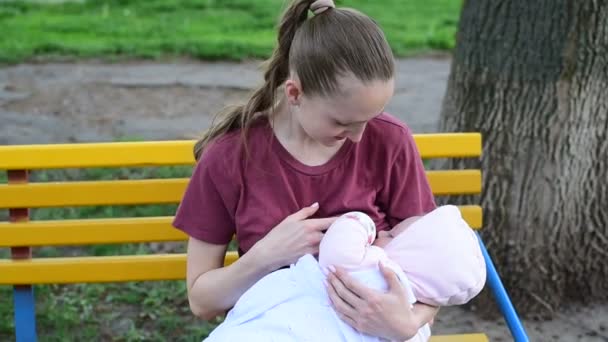 Jonge moeder zit in Park met baby in haar armen en borstvoeding. Baby eten moeders melk buiten. - Video