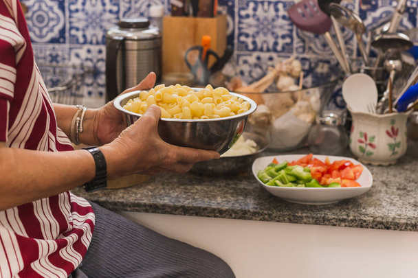 Mujer anciana sosteniendo tazón con pasta de macarrones en la cocina
 - Foto, imagen