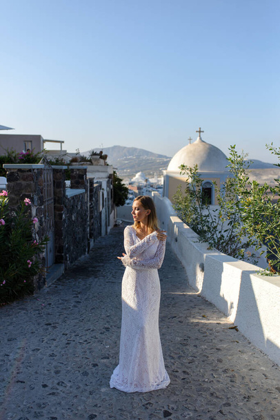 Thira şehrinin arka planında poz veren beyaz elbiseli güzel gelin, Santorini. - Fotoğraf, Görsel