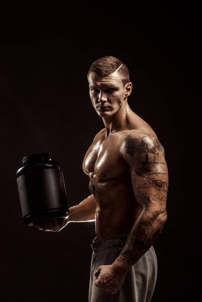Sport backgrounds. Strong bodybuilder holding a plastic jar with a dry protein Isolated. Sport food - Foto, afbeelding