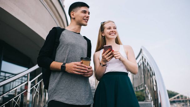 Millennial male and female bloggers looking away and waiting fellow for discussing idesd for funny publication in mobile social network, happy friends enjoying live communication on urban setting - Zdjęcie, obraz