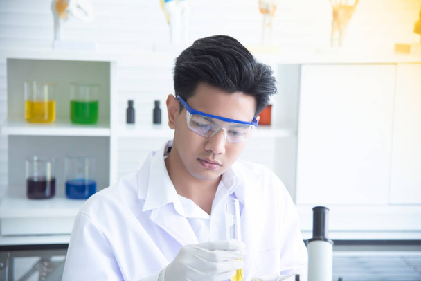 Młody naukowiec azjatycki bada eksperyment, aby wylać chemikalia do wykorzystania w produkcji. Spójrz na probówki w laboratorium naukowym.. - Zdjęcie, obraz