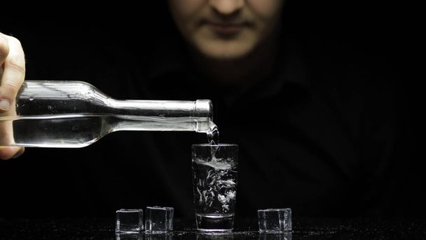Barman pour frozen vodka from a bottle into a glass with ice. Black background - Foto, imagen