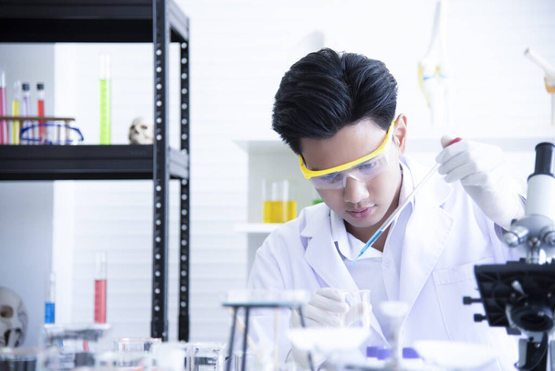 Il giovane scienziato asiatico sta studiando l'esperimento per versare sostanze chimiche da utilizzare nella produzione. Guarda le provette in un laboratorio scientifico
. - Foto, immagini