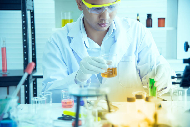 Asyalı genç bilim adamı, kimyasalların üretiminde kullanılmasını araştırıyor ve test ediyor. Bilim laboratuvarlarında test tüpleri, icatlar ve araştırma kavramları. - Fotoğraf, Görsel