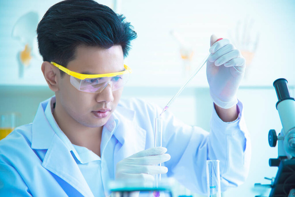 Científico joven asiático está investigando y probando el uso de productos químicos para la producción. Ver tubos de ensayo en laboratorios científicos, inventos y conceptos de investigación
. - Foto, Imagen