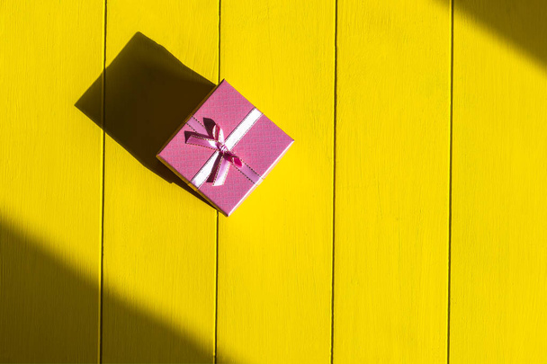 Rough shadow. Retro yellow wooden background. Gift box in pink. - 写真・画像