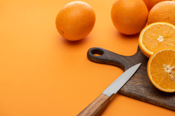świeże soczyste całe i cięte pomarańcze na desce tnącej z nożem na kolorowym tle - Zdjęcie, obraz