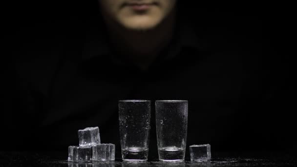 Barmann gießt gefrorenen Wodka aus der Flasche in zwei Gläser mit Eis. Schwarzer Hintergrund - Filmmaterial, Video