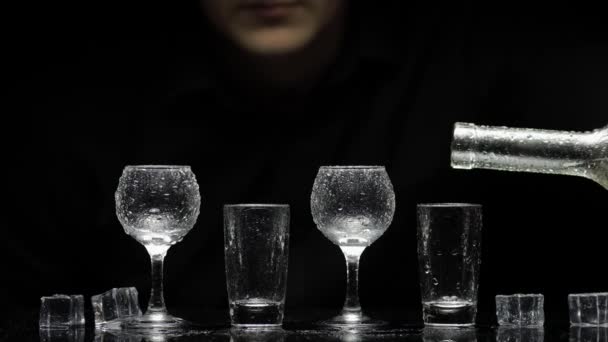 Barman giet bevroren wodka uit de fles in glazen met ijs. Zwarte achtergrond - Video