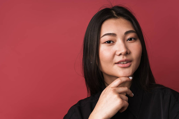 Close up of a pretty smiling young asian woman wearing casual clothes standing isolated over red background, looking at camera - Valokuva, kuva