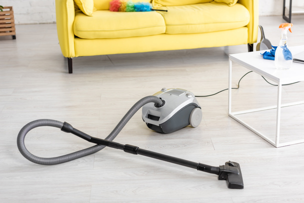 Vacuum cleaner near coffee table and sofa with feather duster in living room - Fotó, kép