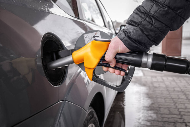 A man's hand holds a yellow refueling gun inserted into the opening of the car's gas tank when refueling with gasoline. Close-up of the hand and the fuel gun. The background is blurred. - Photo, Image