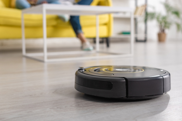 Cropped view of mother with daughter on sofa and robotic vacuum cleaner on floor in living room - Foto, immagini