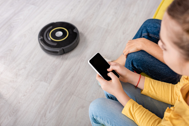 Cropped view of child with smartphone and mother near robotic vacuum cleaner on floor in living room - Φωτογραφία, εικόνα