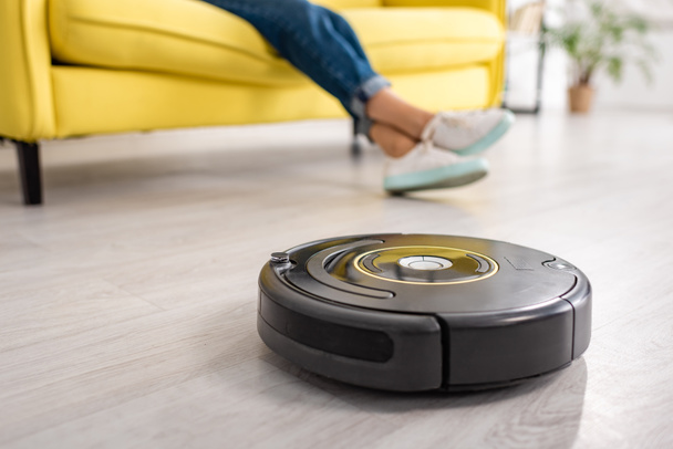 Cropped view of female legs with robotic vacuum cleaner on floor in living room - Foto, immagini