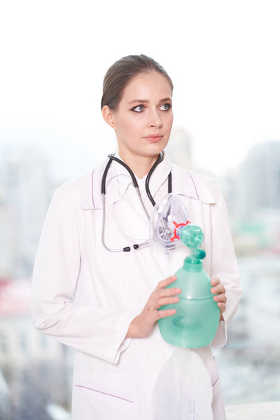  Portrait d'une jeune femme médecin tenant un ventilateur à la main, sur fond blanc, elle regarde ailleurs
                               - Photo, image