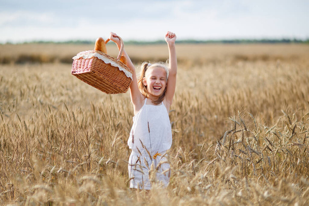 Девушка стоит на пшеничном поле, в белом платье, на закате, летом, с корзиной в руках, хлебом, булочкой, мукой, бубликом, хлебом из хлопьев
 - Фото, изображение