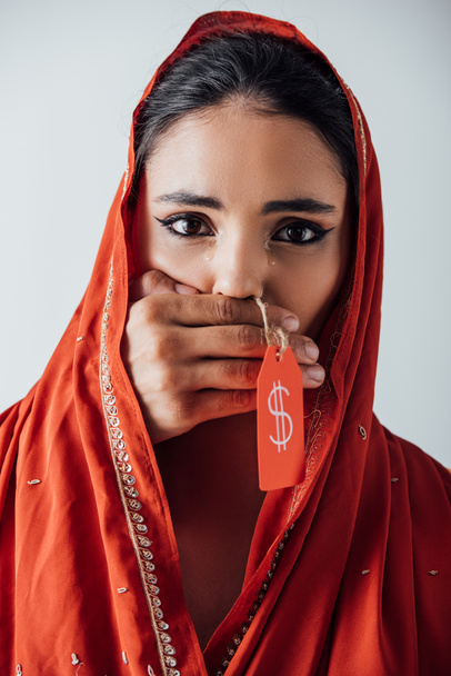 Male hand holding price tag with dollar sign and covering mouth to crying indian woman in sari isolated on grey  - Photo, Image