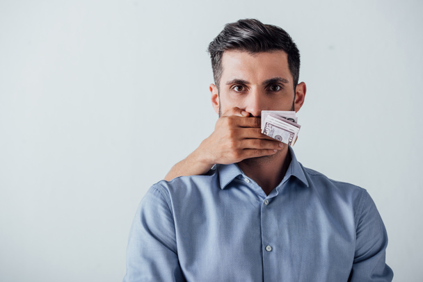 Mano masculina sosteniendo billetes de dólar y cubriendo boca a hombre aislada en gris
 - Foto, Imagen