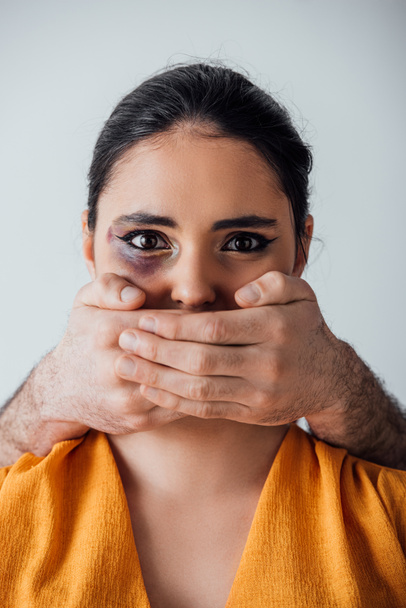 Mãos masculinas cobrindo boca para mulher indiana com hematomas isolados em cinza
 - Foto, Imagem