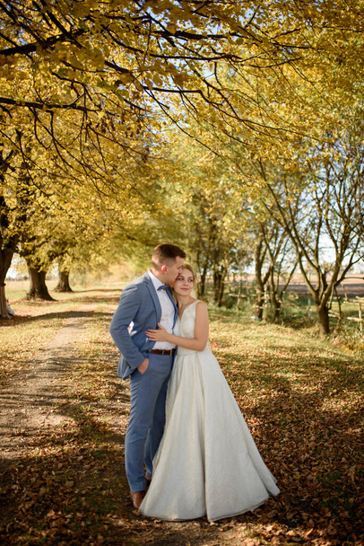 Young beautiful couple hugging in their wedding dresses in autumn park. - Photo, Image
