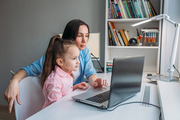 A mãe e a filha estão em casa hoje. Eles trabalham remotamente em um laptop. Mãe ajuda sua filha a completar tarefas em um computador
. - Foto, Imagem