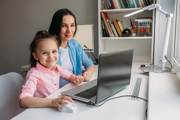 Mom and daughter are at home today. They work remotely on a laptop. Mom helps her daughter complete tasks on a computer. - 写真・画像