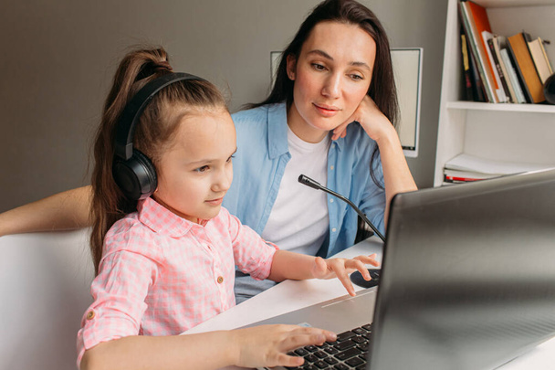 Mom and daughter are at home today. They work remotely on a laptop. Mom helps her daughter complete tasks on a computer. - 写真・画像