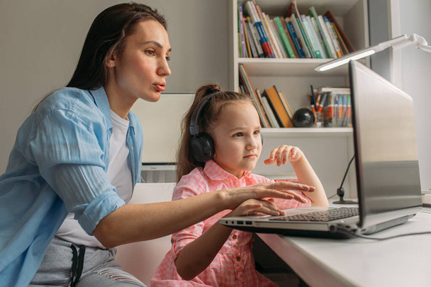 Mama i córka są dziś w domu. Pracują zdalnie na laptopie. Mama pomaga córce wykonać zadania na komputerze. - Zdjęcie, obraz