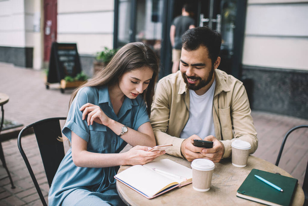Multicultural couple in love checking notification on cellular phones while spending time in coffee shop for learning togetherness with textbooks for education, millennial friends chatting on website - Fotografie, Obrázek