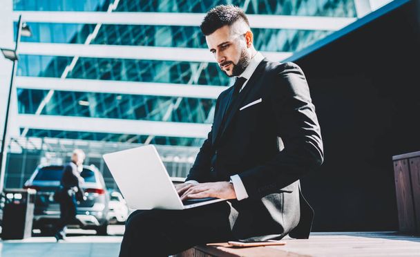 Side view of successful male boss of company using laptop for searching financial document on company website using public internet for working, intelligent trader updating information on web page - Foto, Imagen