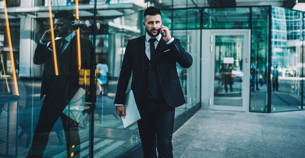Half length portrait of serious Caucasian economist with netbook looking at camera and walking to business meeting, confident entrepreneur making call to banking operator for checking balance - Фото, изображение